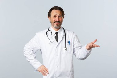 Covid-19, koronavirüs salgını, sağlık çalışanları ve pandemik konsept. Şüpheci ve kafası karışmış beyaz önlüklü erkek doktor, korku ve ironi dolu, suratını buruşturan hayal kırıklığı