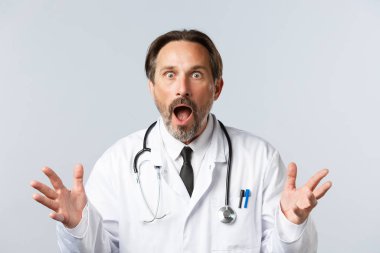 Covid-19, virüsü önleme, sağlık çalışanları ve aşı konsepti. Şok olmuş ve endişeli doktor beyaz önlüklü. Çenesi düşmüş, soluk soluğa kalmış. Kötü haberleri duyun, korkuyla el kaldırın.