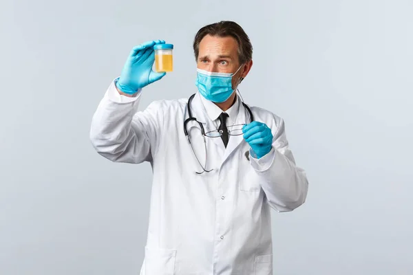 Covid-19, prévention du virus, personnel de santé et concept de vaccination. Médecin sérieux dans le masque médical et les gants examiner l'échantillon d'urine, l'air réfléchi et concentré — Photo