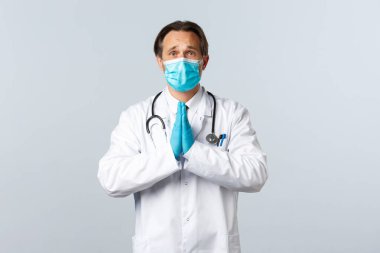 Covid-19, virüsü önleme, sağlık çalışanları ve aşı konsepti. Umut dolu, tıbbi maskeli ve eldivenli doktor. Dua ederken, kaşlarını çatarken, iyilik isterken.