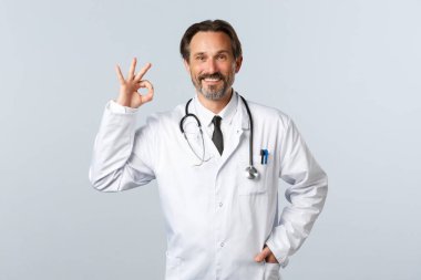 Covid-19, koronavirüs salgını, sağlık çalışanları ve pandemik konsept. Kendine güvenen erkek doktor, klinikteki profesyonel terapist kaliteyi tavsiye etmek veya garantilemek için iyi bir hareket gösteriyor.