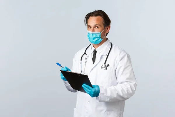 Covid-19: 바이러스 예방, 의료 종사자 및 예방 개념. 의료용 마스크와 장갑을 끼고, 클립보드를 들고, 환자 증상을 적고, 클리닉에서 코로나 바이러스와 싸우는 전문 의사 — 스톡 사진