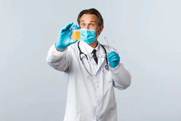 Covid-19: 바이러스 예방, 의료 종사자 및 예방 개념. 흥분 한 실험실 과학자 이자 진료소의 의사는 의료용 마스크와 환자의 소변 샘플을 보여 주는 장갑을 착용 한다 — 스톡 사진