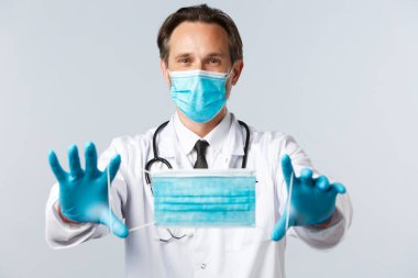 Covid-19, virüs, sağlık çalışanları ve aşı konsepti. PPE 'deki doktor ellerini uzattı ve hasta maskesi taktı. Koronavirüs disesaz' ına karşı önleyici önlemler alınmasını tavsiye etti.