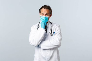 Covid-19, virüsü önleme, sağlık çalışanları ve aşı konsepti. Tıbbi maskeli ve eldivenli düşünceli, ciddi bir erkek doktor. Düşünüyor, karar veriyor ya da karar veriyor.
