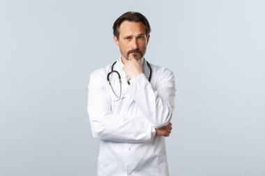 Covid-19, koronavirüs salgını, sağlık çalışanları ve pandemik konsept. Düşünceli ciddi bir doktor karar veriyor, hasta vakasına odaklanmış gibi görünüyor. Hekim varsayımda bulunuyor