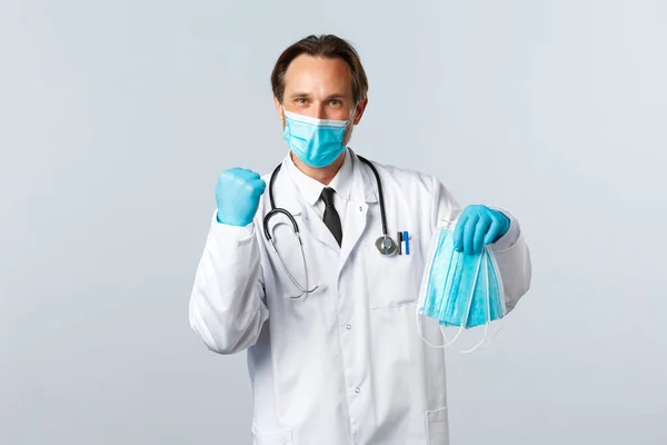 Covid-19, πρόληψη του ιού, εργαζόμενοι στον τομέα της υγείας και την έννοια του εμβολιασμού. Εύθυμη γιατρός στην κλινική φορώντας ΜΑΠ έλαβε ιατρικές μάσκες για τους υπαλλήλους του νοσοκομείου, στέκεται λευκό φόντο — Φωτογραφία Αρχείου