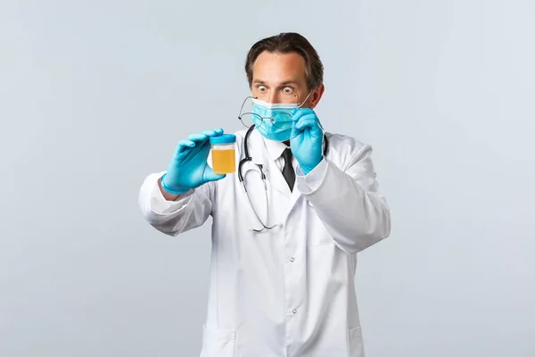 Covid-19: 바이러스 예방, 의료 종사자 및 예방 개념. 의료용 마스크와 장갑을 끼고 진료소에서 일하는 충격적 인 의사가 소변 샘플을 보고 깜짝 놀란 모습 — 스톡 사진