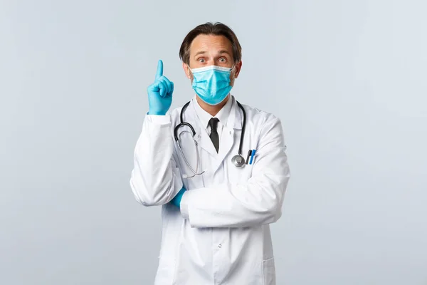 Covid-19: 바이러스 예방, 의료 종사자 및 예방 개념. 의료용 마스크와 장갑을 착용하고 있는 흥분 한 남성 의사는 코로나 바이러스 환자에 대한 해결책을 제시하면서 손가락을 들어 본다 — 스톡 사진