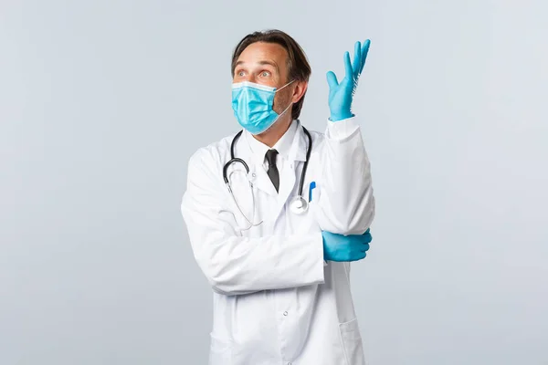 Covid-19, πρόληψη του ιού, εργαζόμενοι στον τομέα της υγείας και την έννοια του εμβολιασμού. Ενθουσιασμένος αισιόδοξος άνδρας γιατρός με ιατρική μάσκα και γάντια, σηκώνοντας το χέρι στοχαστικός, έχουν ιδέα, φαίνονται έκπληκτοι — Φωτογραφία Αρχείου