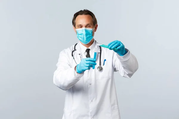 Covid-19, mencegah virus, pekerja kesehatan dan konsep vaksinasi. Smiling doctor in medical mask and gloves tuangkan chemical ingridient into another test-tube, conducting vaccine tests — Stok Foto