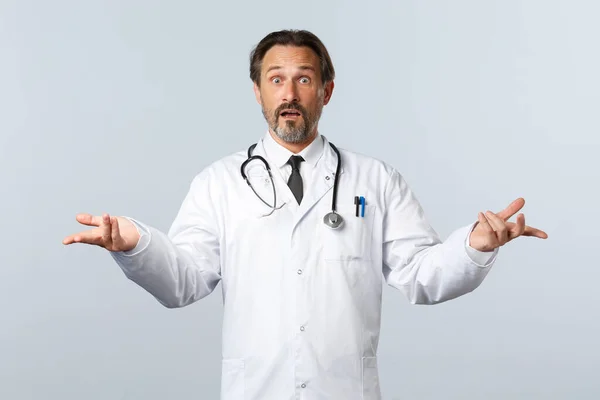 Covid-19, coronavirus outbreak, healthcare workers and pandemic concept. Worried indecisive male doctor in white coat, pointing hands sideways at variants and stare confused, cant decide — Stock Photo, Image