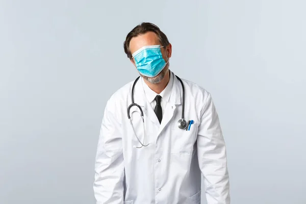 Covid-19: 바이러스 예방, 의료 종사자 및 예방 개념. 피곤 하고 피곤 한 의사는 얼굴 전체에 마스크를 쓰고 탈진하여 하얀 배경을 가진 채 몸을 굽힌다 — 스톡 사진