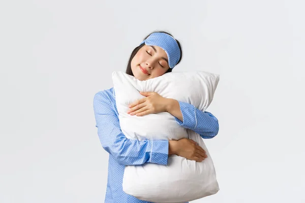 Kawaii azjatycka dziewczyna w masce snu i piżamy przytulając wygodną poduszkę z zamkniętymi oczami. Kobieta w piżamie dobrze sypia, czuje się uradowana leżąc w łóżku po produktywnym dniu — Zdjęcie stockowe