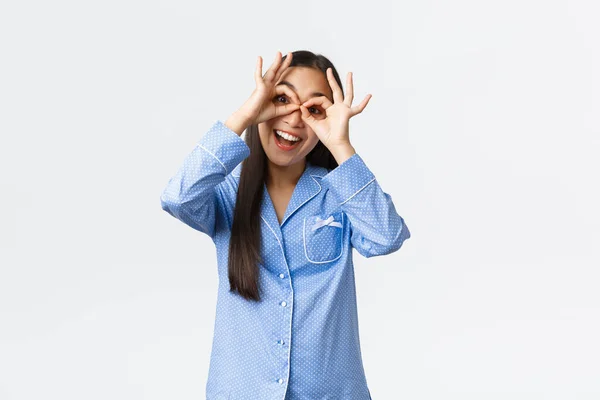 Glückliche schöne asiatische Mädchen im blauen Pyjama zeigt gefälschte Brille Geste und lächelt optimistisch, Spaß mit Geschwistern auf Slepover-Party, trägt Jammies und Narr herum, weißer Hintergrund — Stockfoto