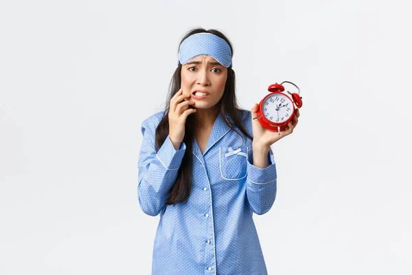 Ansioso bonito asiático menina mostrando alarme e pânico, mordendo o dedo preocupado, olhando nervoso, não sei o que fazer por estar atrasado, adormeceu para o trabalho de manhã, vestindo pijama e máscara de dormir — Fotografia de Stock