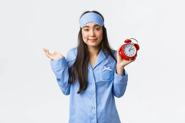 Sem incomodado bonito ásia menina no dormir máscara e pijama mostrando alarme relógio e encolhendo descuidado, overslept mas don 't dar damn, don' t cuidado para ser tarde, pé branco fundo — Fotografia de Stock