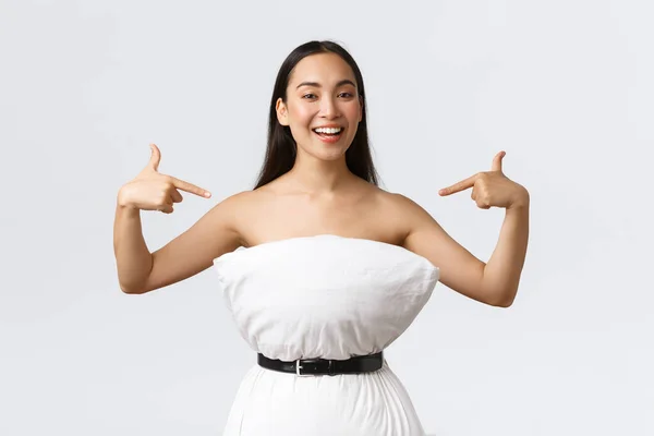 Όμορφη χαμογελαστή γυναίκα blogger συμμετέχει σε πρόκληση μαξιλαριών, ασφαλές μαξιλάρι με ζώνη γύρω από τα απόβλητα σαν να φοράει μαξιλάρι φόρεμα, δείχνοντας τον εαυτό της, στέκεται λευκό φόντο — Φωτογραφία Αρχείου