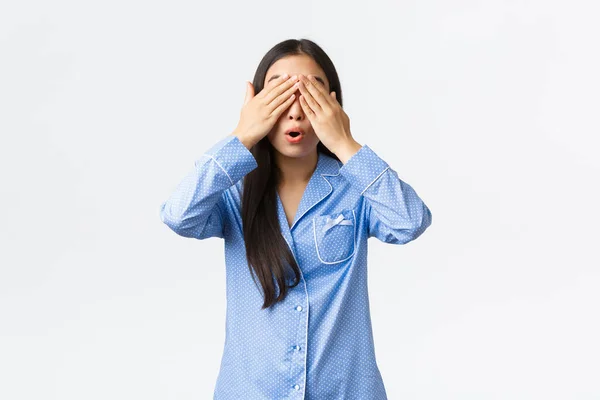 Meglepett és izgatott aranyos ázsiai lány kék pizsamában csukott szemmel és nyitott szájjal izgatott, várja a meglepetés ajándék, vár a jel, álló pizsama fehér háttér — Stock Fotó