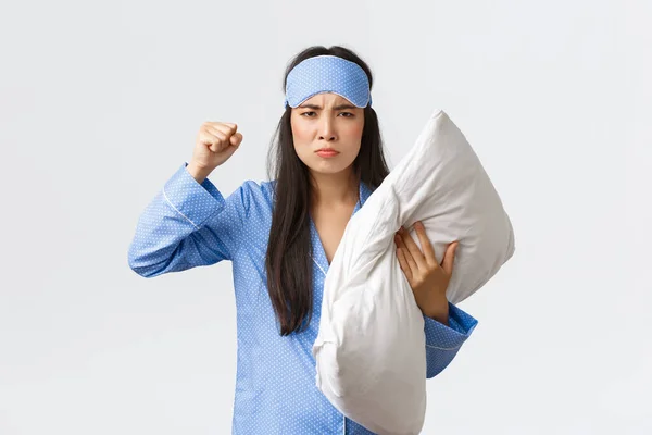 Angry and bothered exhausted asian girl complaining loud neighbours at dormitory, wearing sleeping mask and pajama, hold pillow and threaten someone as cant sleep, scolding people being too loud — Stock Photo, Image