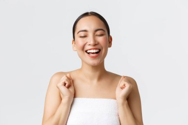 Güzellik, kozmetoloji ve kaplıca salonu konsepti. Mutlu, muhteşem Asyalı bir kadının banyo havlusuyla yakın çekimi. Gözlerinizi kapatın ve neşe içinde gülün. Güzellik kliniğinin reklamı, masaj terapisi.