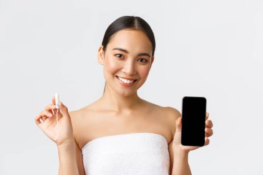 Güzellik, kişisel ve samimi bakım, mobil uygulama konsepti. Havlu giymiş çekici bir Asyalı kadın tampon ve adet döngüsü gösteriyor. Akıllı telefon uygulaması ekranında, beyaz arka planda duruyor.