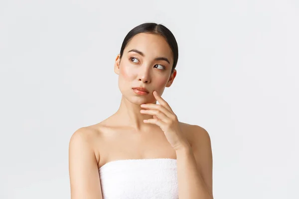 Kecantikan, kosmetologi dan konsep salon spa. Wanita asia cantik yang bijaksana dengan handuk melihat ke kiri dan berpikir, merenungkan atau membuat pilihan prosedur yang diambil di klinik kecantikan — Stok Foto