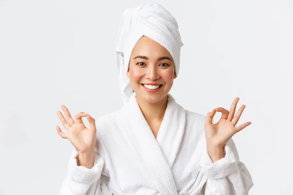 Cuidados pessoais, mulheres beleza, banho e chuveiro conceito. Close-up de aliviado atraente mulher asiática assistir spa salão de beleza, use toalha de banho e roupão de banho, meditando, sentindo nirvana, sorrindo — Fotografia de Stock