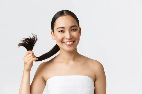 Kecantikan, produk rambut rontok dan konsep perawatan rambut. Gadis asia yang cantik dengan handuk mandi menunjukkan rambut dan tersenyum puas, merekomendasikan sampo atau kondisioner, berdiri latar belakang putih — Stok Foto