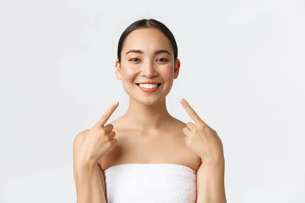 Kecantikan, kosmetologi dan konsep salon spa. Close-up of happy asian woman with white perfect gigings, clean skin pointing at face with pleased grin, satisving with cosmetic prosedur in beauty clinic — Stok Foto