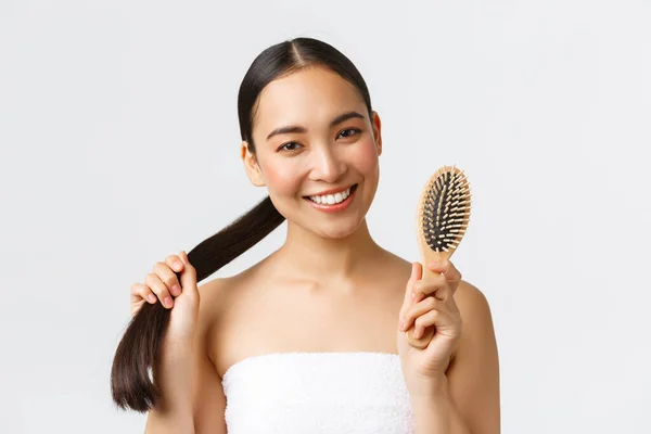 Kecantikan, produk rambut rontok, sampo dan konsep perawatan rambut. Close-up dari senang menarik perempuan asia di handuk mandi menunjukkan sikat, merekomendasikan produk perawatan rambut untuk rambut panjang yang sehat — Stok Foto