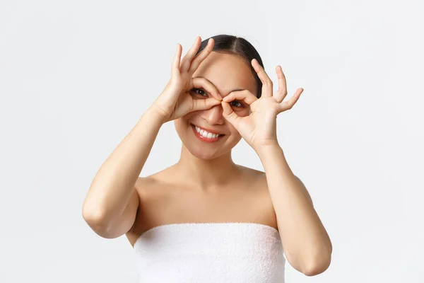 Kecantikan, kosmetologi dan konsep salon spa. Close-up of playful pretty asian woman in bath towns smile wide and making fake glasses with hands over eyes, looking upbeat at camera — Stok Foto