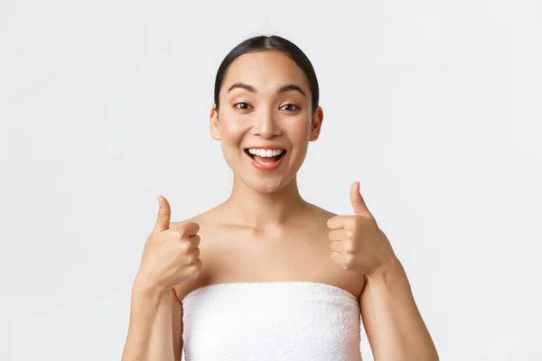Beauty, cosmetology and spa salon concept. Excited upbeat asian girl in towel around body showing thumbs-up and smiling pleased, recommend massage therapy, beauty salon services, white background — Stock Photo, Image