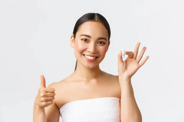 Kecantikan, pribadi dan intim perawatan konsep kebersihan menstruasi. Close-up of beautiful young asian woman in bath towns shows tampon and thumbs-up, being on her peirod, white background — Stok Foto