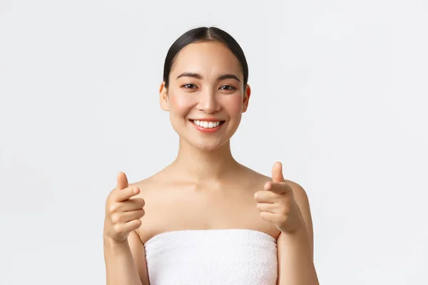 Beauty, cosmetology and spa salon concept. Close-up or attractive asian woman in towel smiling happy and pointing finger at camera, recommend you visit beauty clinic, white background — Stock Photo, Image