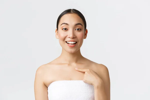 美容美发和温泉沙龙的概念。用白色毛巾微笑着对满意的亚裔女性客户进行特写，并对自己指指点点，推荐美容院和护肤程序 — 图库照片
