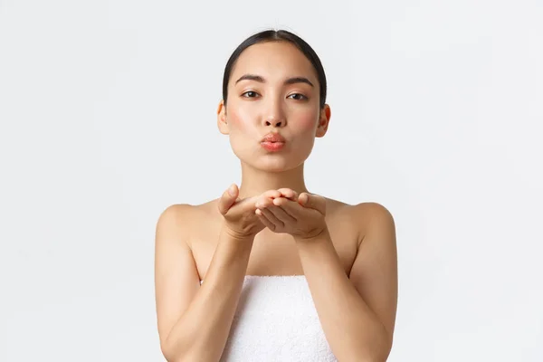 Sexig feminin asiatisk flicka i handduk skicka luft kyss försiktigt vid kameran, promo erbjudande av hudvårdsprodukter, schampo eller ansiktsrengöring. Kvinna stående i badrummet och blåser mwah — Stockfoto