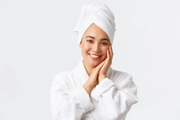 Personlig vård, kvinnlig skönhet, bad och dusch koncept. Närbild av vacker glad asiatisk kvinna i handduk och badrock röra ansiktet försiktigt, leende vita tänder, främjande av hudvård och hygienprodukter — Stockfoto