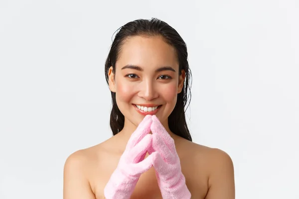 Cuidado personal, belleza de las mujeres, baño y ducha concepto. Primer plano de bonita hembra asiática de pie desnuda en guantes de baño, dedos de campanario reflexivo, haciendo cara complacida, astucia sonriente —  Fotos de Stock