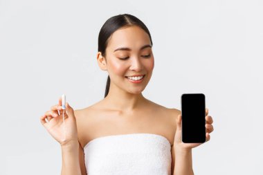 Güzellik, kişisel ve samimi bakım, mobil uygulama konsepti. Tampon tutan ve periyot takip cihazı ve adet döngüsü uygulaması olan akıllı telefon ekranına bakan kendinden emin Asyalı kız.