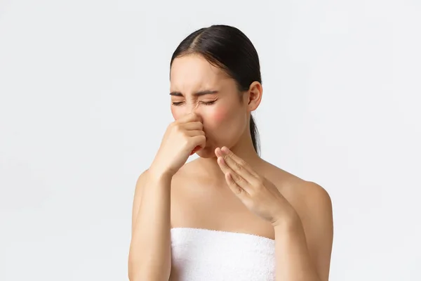 Skønhed, kosmetologi og spa salon koncept. Close-up af smuk asiatisk kvinde hader lugt af aromaterapi olie, stående i badehåndklæde under massage og dække næse i afsky, hvid baggrund - Stock-foto