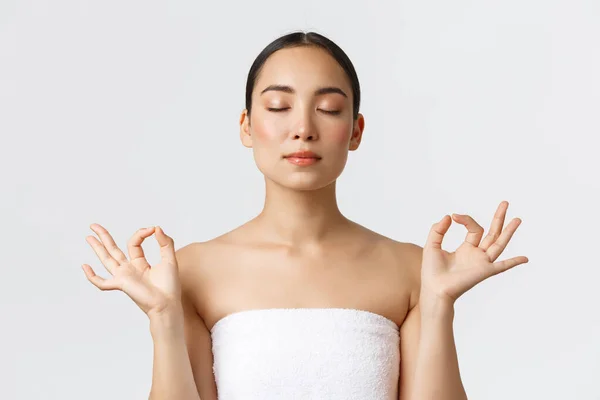 Kecantikan, kosmetologi dan konsep salon spa. Close-up of meditating relaxed beautiful asian female in white towns make zen gestur with closed eyes, feeling pleasure after massage therapy — Stok Foto