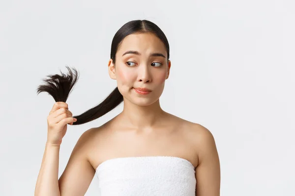 Beleza, produtos de perda de cabelo, shampoo e conceito de cuidados com o cabelo. Perturbado bela mulher asiática na toalha de banho olhando pontas duplas, precisa de tratamento de cabelo, de pé fundo branco — Fotografia de Stock