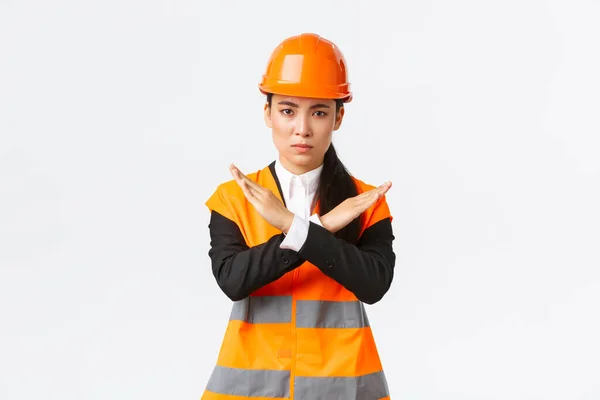 Ernstig uitziende Aziatische vrouwelijke baas, bouwmanager in veiligheidshelm toont kruis gebaar om te stoppen, verbieden gevaarlijke actie, teleurgesteld met resultaat, verbieden iets — Stockfoto