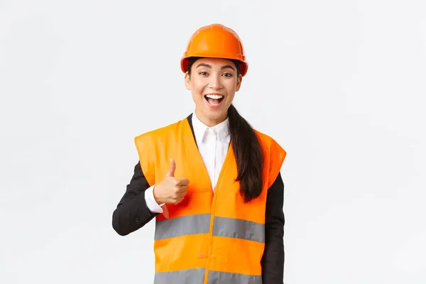 Supportive and pleased happy asian female chief engineer in safety helmet showing thumbs-up in approval, satisfied with construction work. Industrial woman in reflecive jacket inspect area — Stock Photo, Image