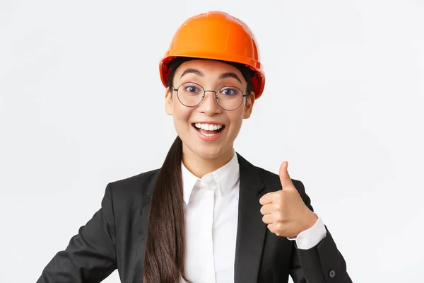 プロの幸せなアジアの女性チーフエンジニア、ビジネススーツと承認で親指アップを示す安全ヘルメットの建築家のクローズアップ、許可を与える、建設会社をお勧めします — ストック写真