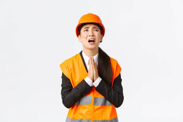 Zoufalá a lehkomyslná asijská stavební manažerka, architektka prosící Boha, nosící bezpečnostní přilbu, držící se za ruce v modlitbě, prosící, prosící Boha o pomoc, prosící o bílé pozadí — Stock fotografie