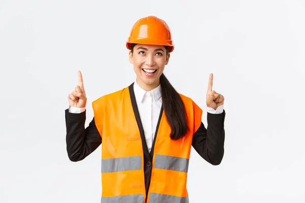 Bouw, bouw en industrieel concept. Succesvolle tevreden Aziatische vrouwelijke ingenieur in veiligheidshelm inspecteren object, kijken en wijzen vingers omhoog tevreden. Architect blij met goed resultaat — Stockfoto