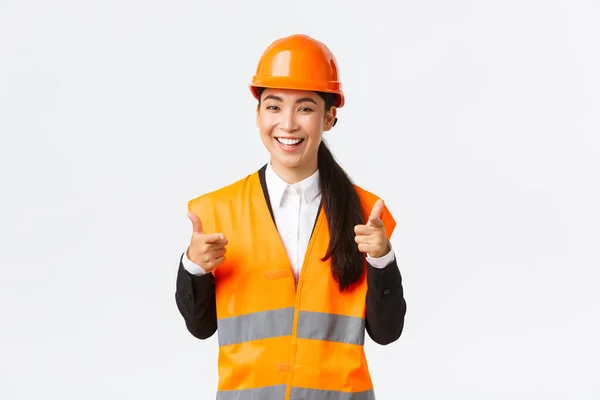 Självsäker ganska asiatisk kvinnlig byggchef i skyddshjälm och reflekterande jacka, pekar finger åt kameran prisar fint val, bra arbete eller bra gjort, stående vit bakgrund — Stockfoto