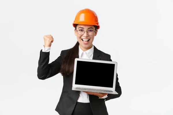Successful winning businesswoman, construction manager or engineer at factory showing profit chart, diagram at laptop screen, fist pump in rejoice, standing pleased over white background — Stock Photo, Image